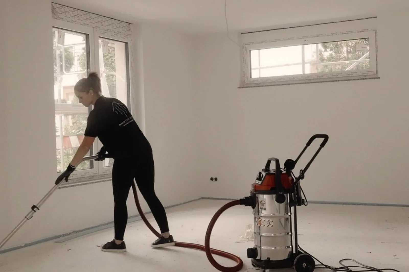 Mitarbeiterin bei der Baureinigung für Bauträger in einem leeren Neubau-Raum mit Industriesauger
