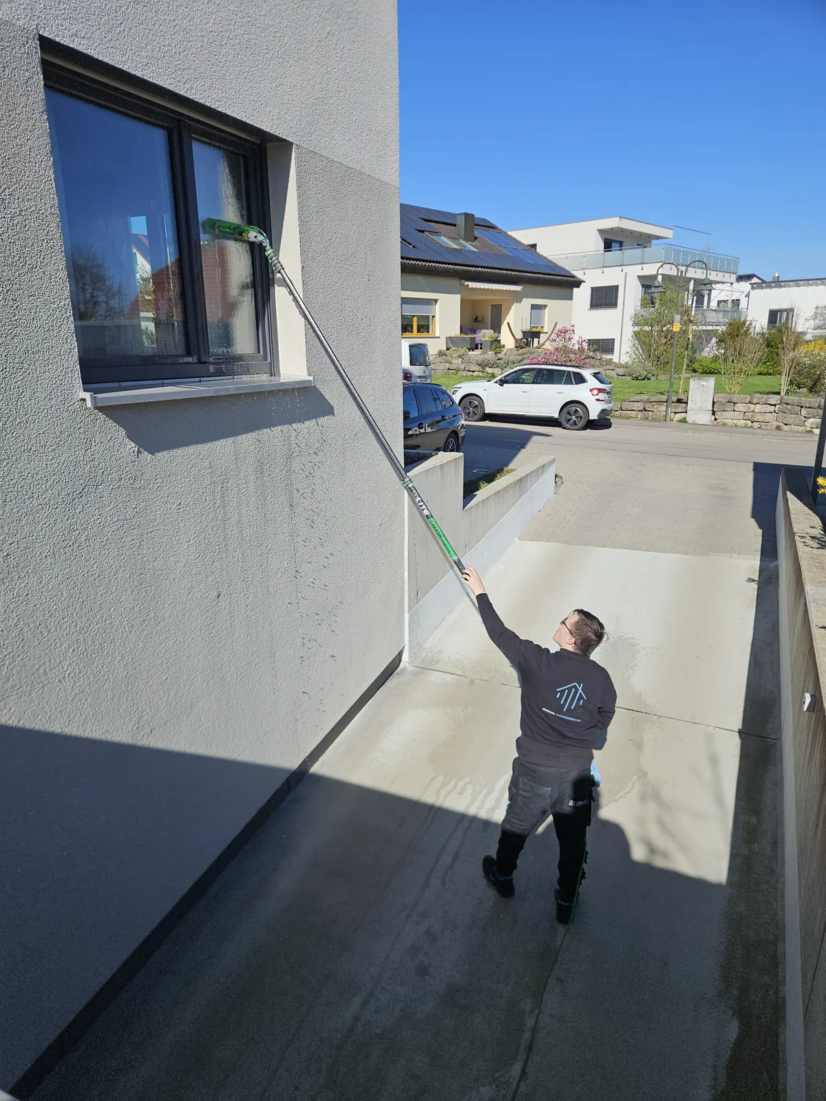 Mitarbeiter reinigt ein Fenster im Obergeschoss mit einer wasserführenden Teleskopstange
