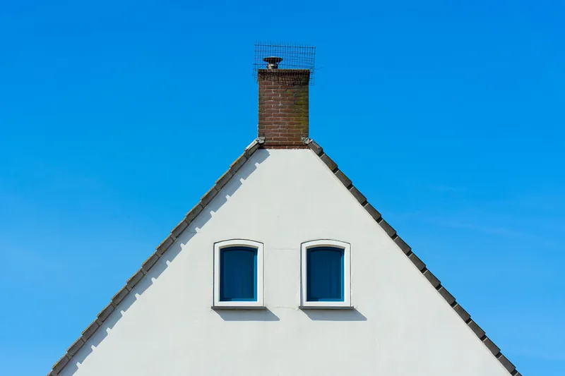 Sauber weiß verputzter Hausgiebel mit zwei Fenstern vor blauem Himmel
