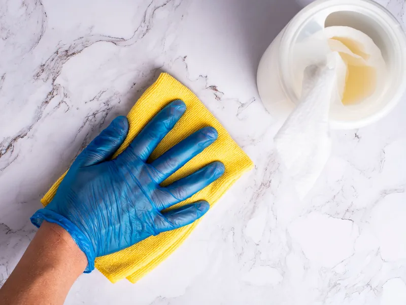 Hand im Handschuh wischt eine weiße Arbeitsfläche mit gelbem Tuch