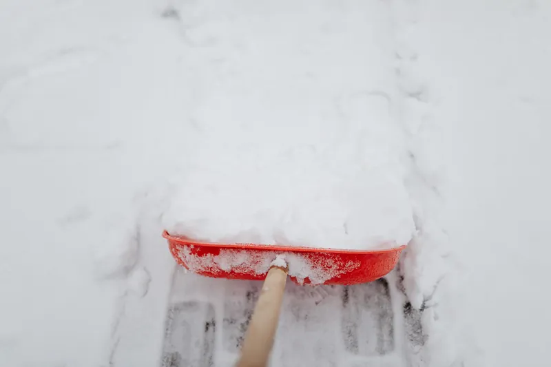 Rote Schneeschaufel schiebt Schnee und legt Pflastersteine frei