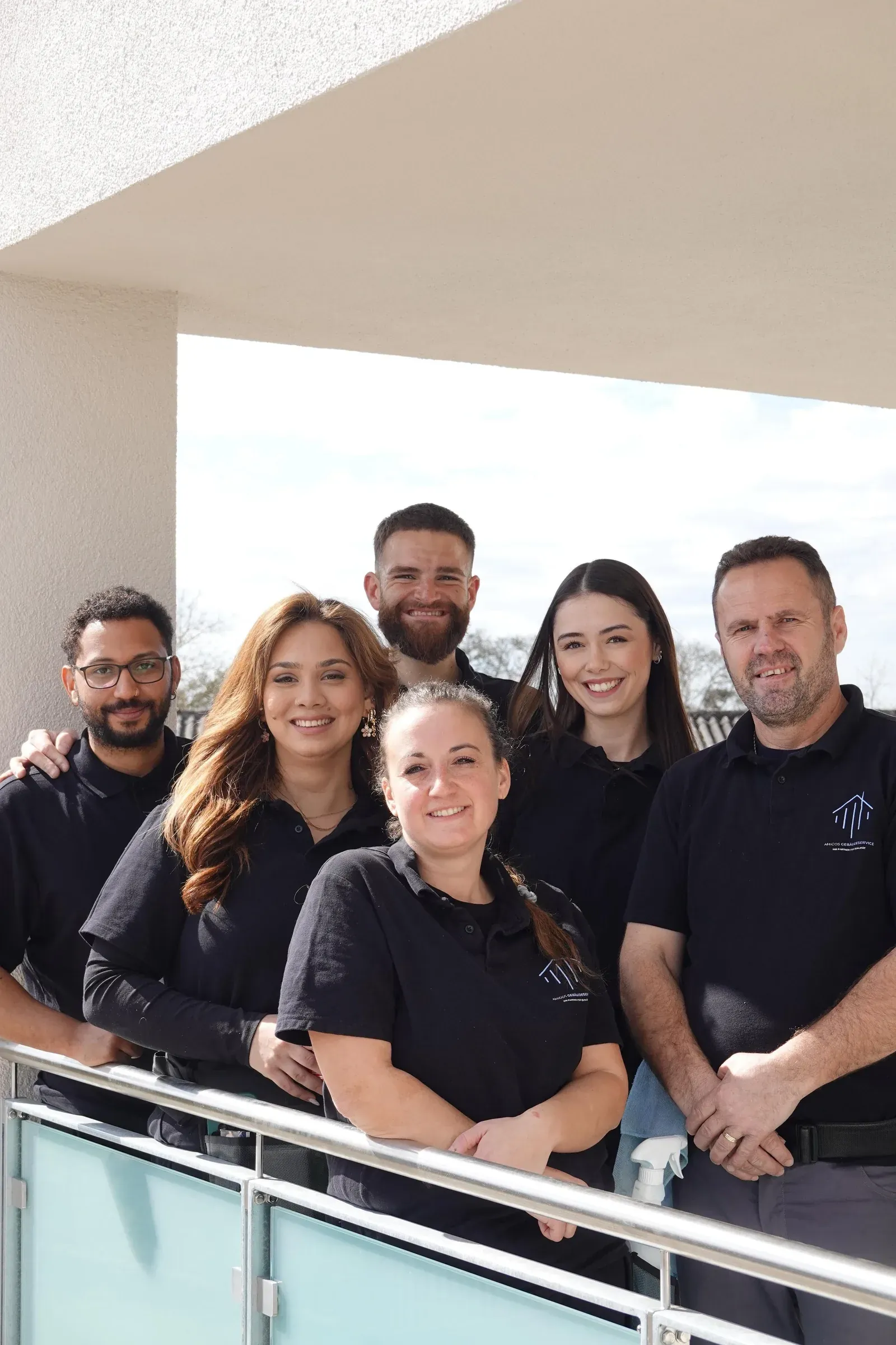 Das Team von Amigos Gebäudeservice lacht gemeinsam an einem Balkongeländer